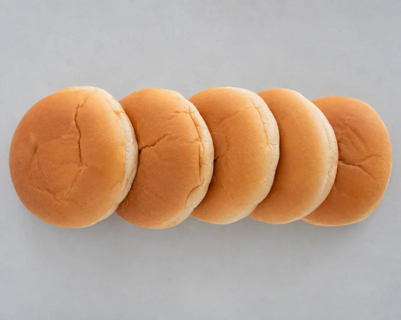 A row of plain burger buns with smooth glazed tops