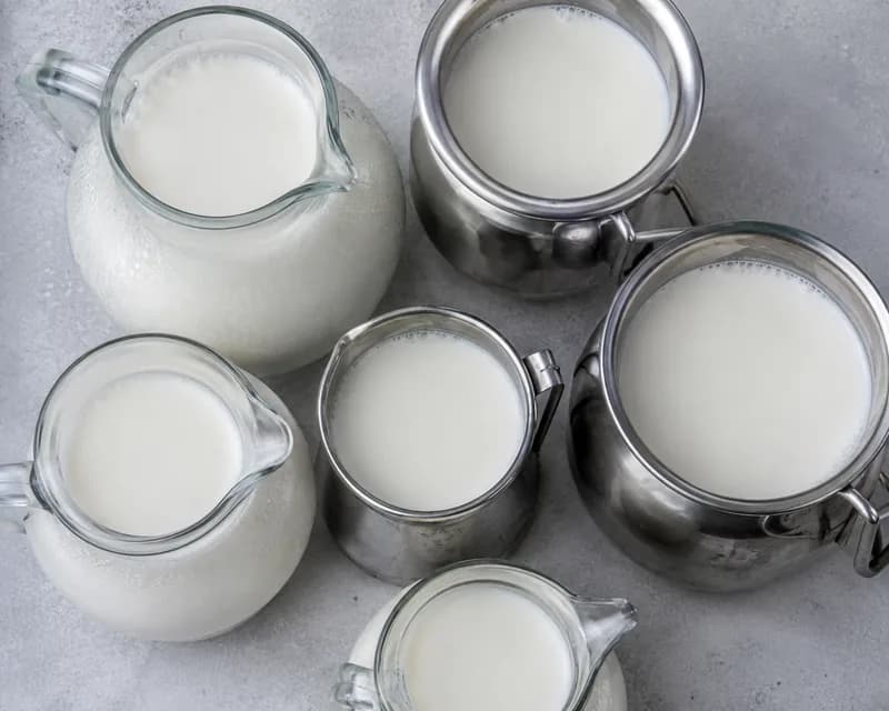 Glass and stainless jugs of fresh whole milk, seen from above