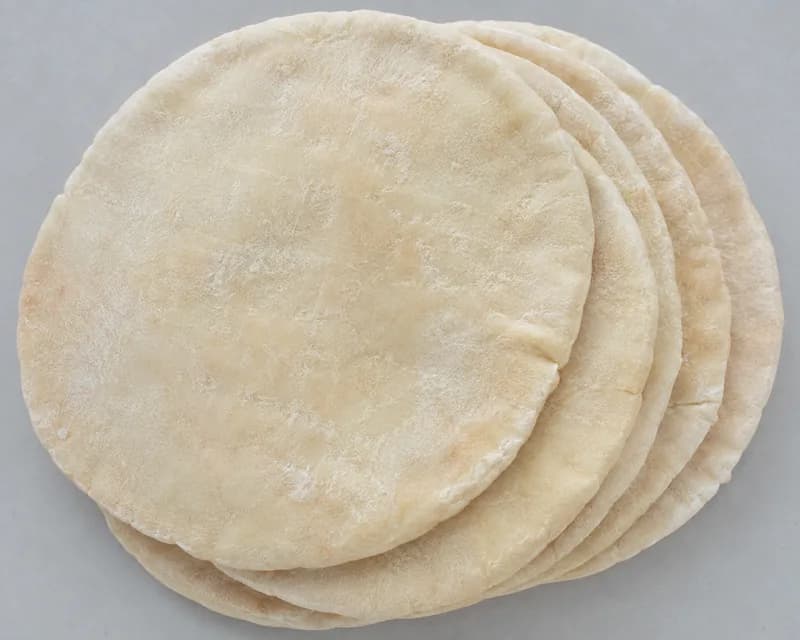 A stack of plain pitta breads dusted with flour