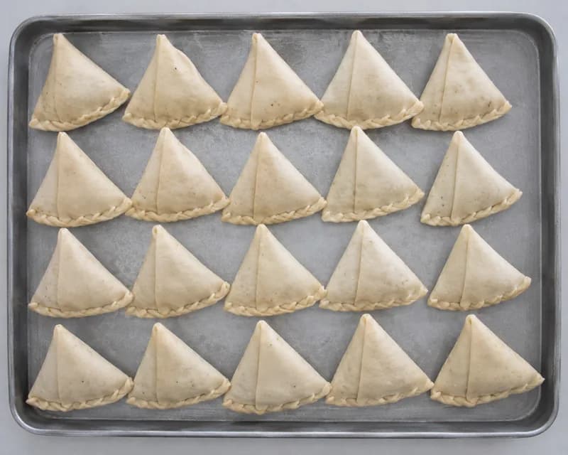 Uncooked folded samosas arranged on a metal baking tray