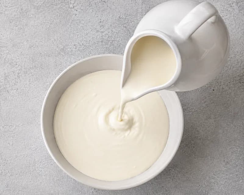 Single cream being poured from a white jug into a shallow bowl